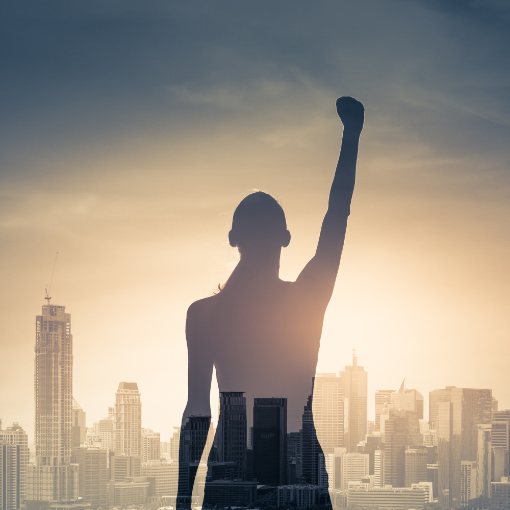 confident young woman with fist in the air facing the city. Peop