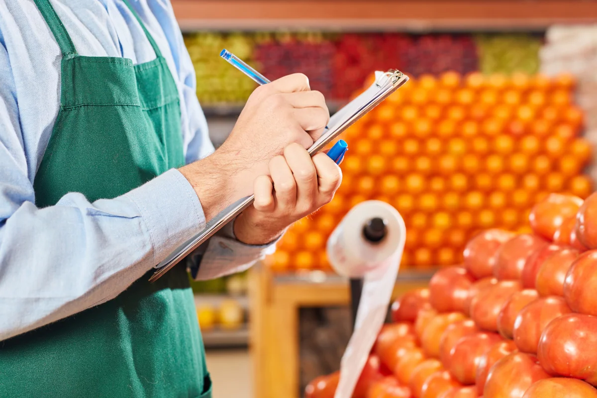 Kaufmann im Supermarkt bei Inventur mit Checkliste in der Gemüseabteilung